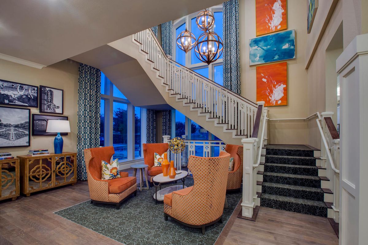 A modern lobby area featuring vibrant orange chairs, a stylish staircase, and colorful artwork on the walls.