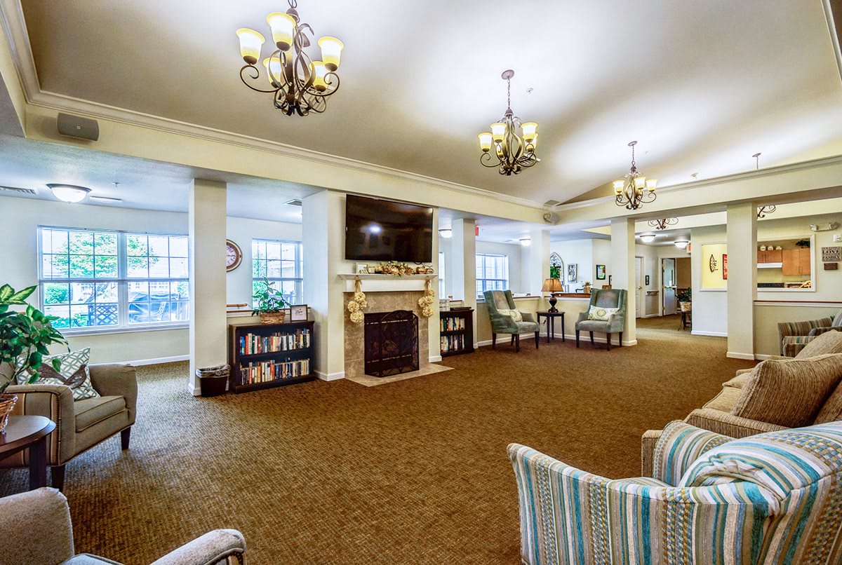 A spacious and elegantly designed living room with chandeliers, a fireplace, bookshelves, and comfortable seating.