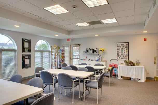 A well-lit meeting room with tables and chairs arranged neatly, featuring large windows and shelving units.