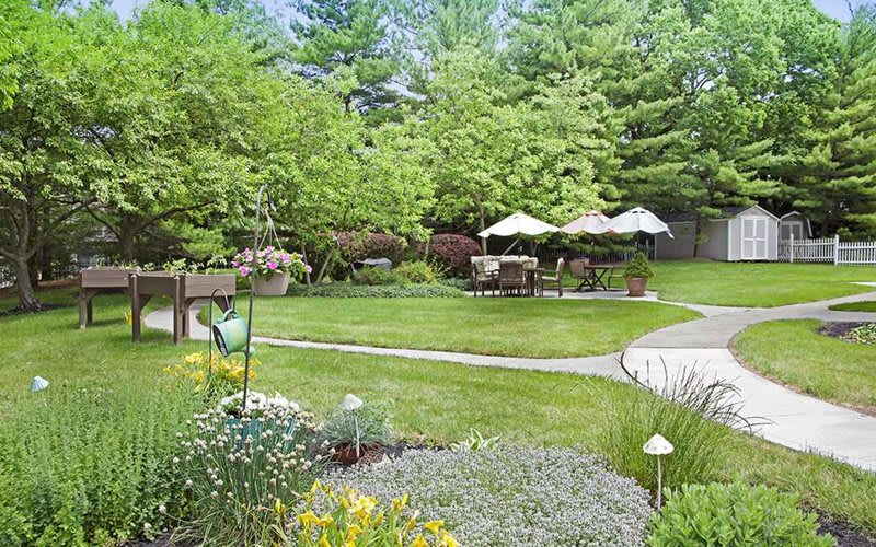 A lush garden with vibrant greenery, featuring patio furniture under umbrellas.