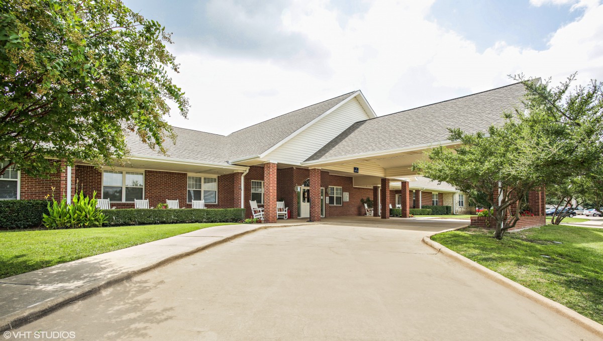 A view of a residential building entrance with a driveway and landscaped surroundings.