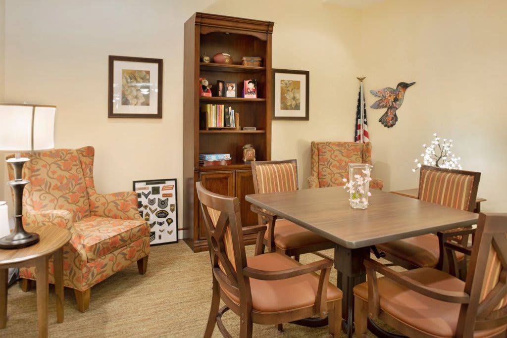 A cozy office space featuring a wooden table with chairs, a bookshelf, and decorative artwork on the walls.