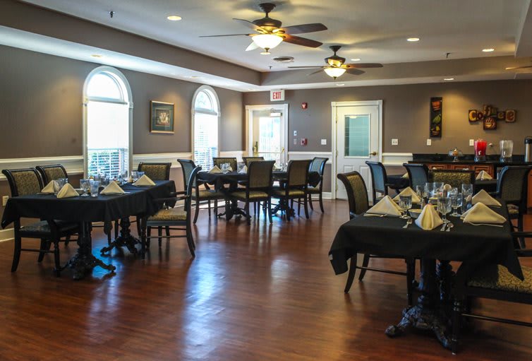 An elegant dining area with neatly arranged tables and chairs, featuring wooden floors and ceiling fans.