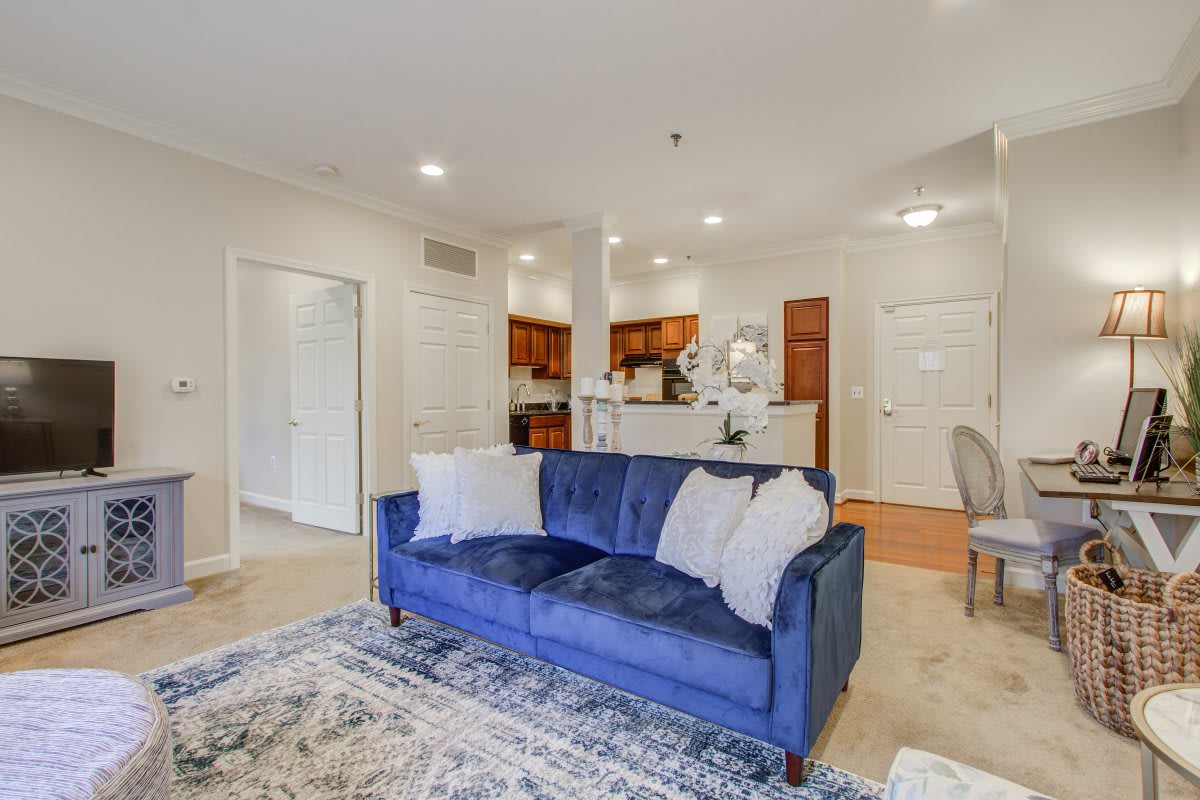 A stylish living room featuring a blue sofa and an open floor plan leading to the kitchen.