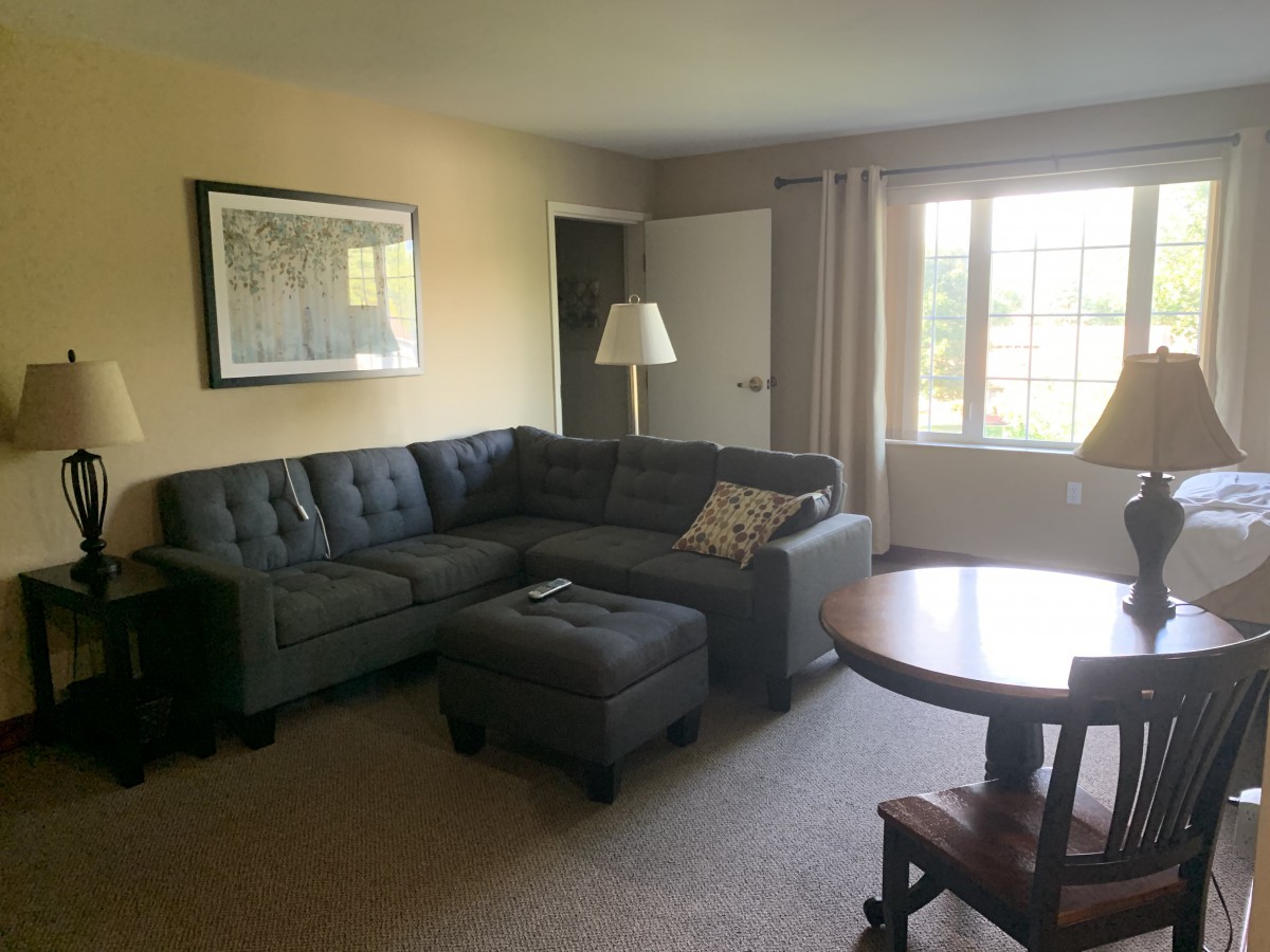 A cozy living room with a sectional sofa, coffee table, and lamp near the window.
