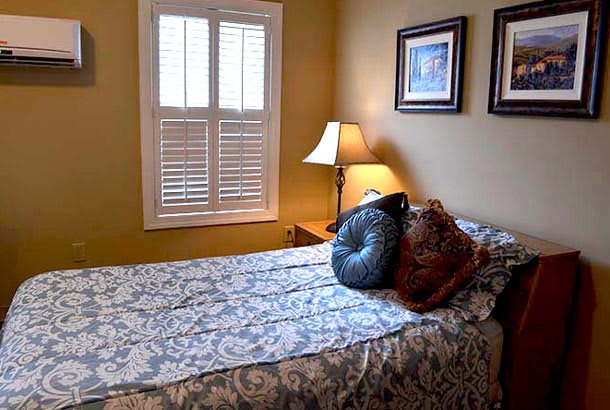 A cozy bedroom with a bed, decorative pillows, a lamp, and framed pictures on the wall.