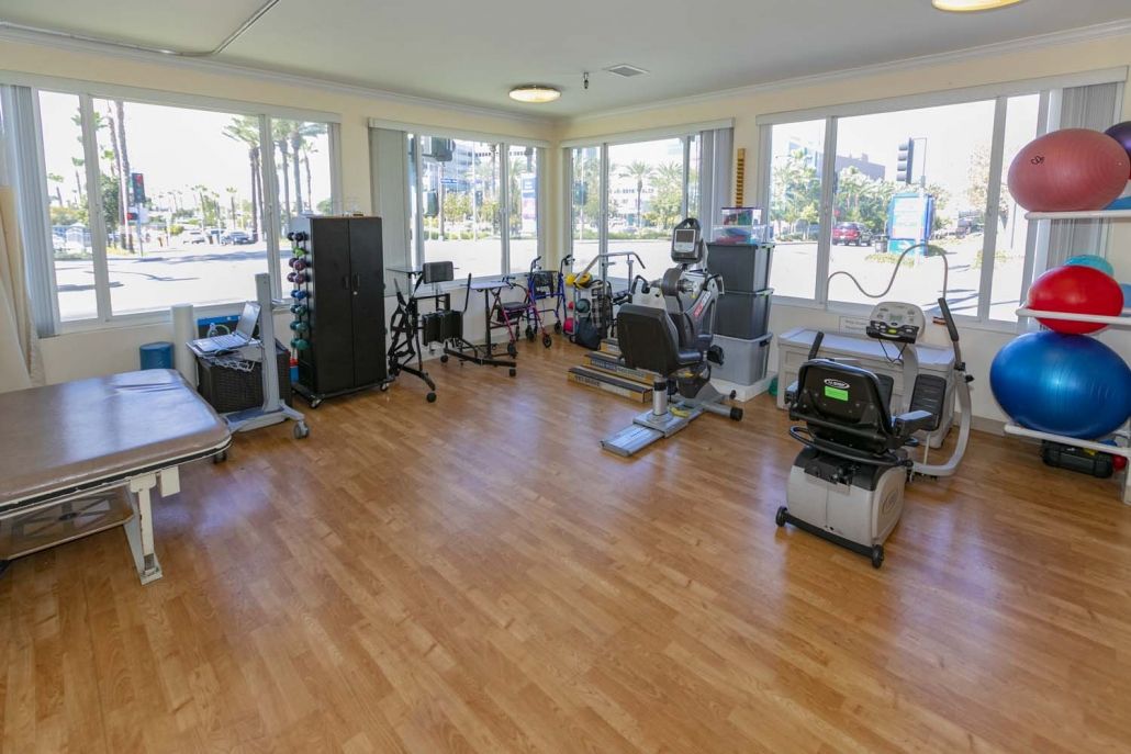 A well-equipped gym with various fitness machines and large windows providing natural light.