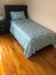 A tidy bedroom with a single bed and patterned bedding on a wooden floor.
