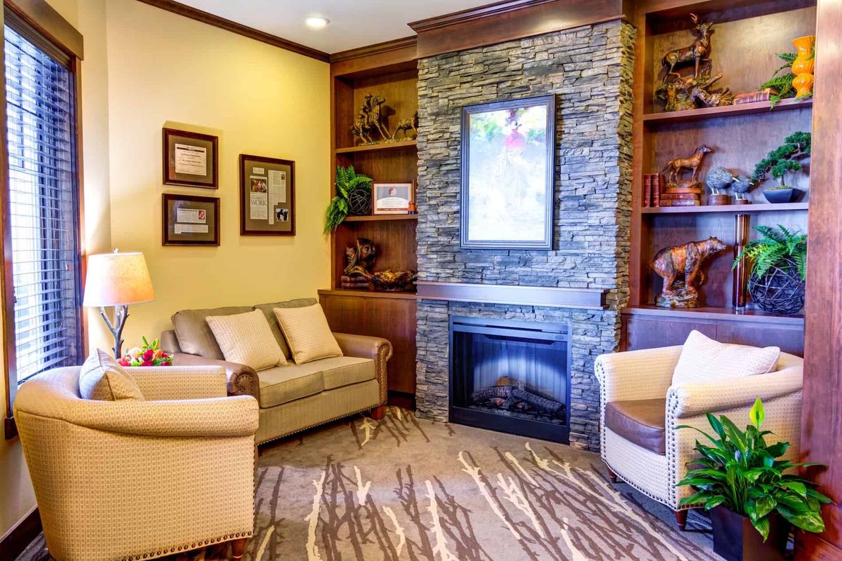 A cozy living room with a stone fireplace, surrounded by a sofa and armchair, and built-in bookshelves.