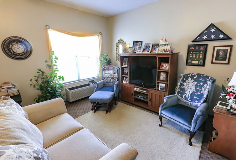 A cozy living room with a sofa, chairs, and a television in front of a bookshelf.