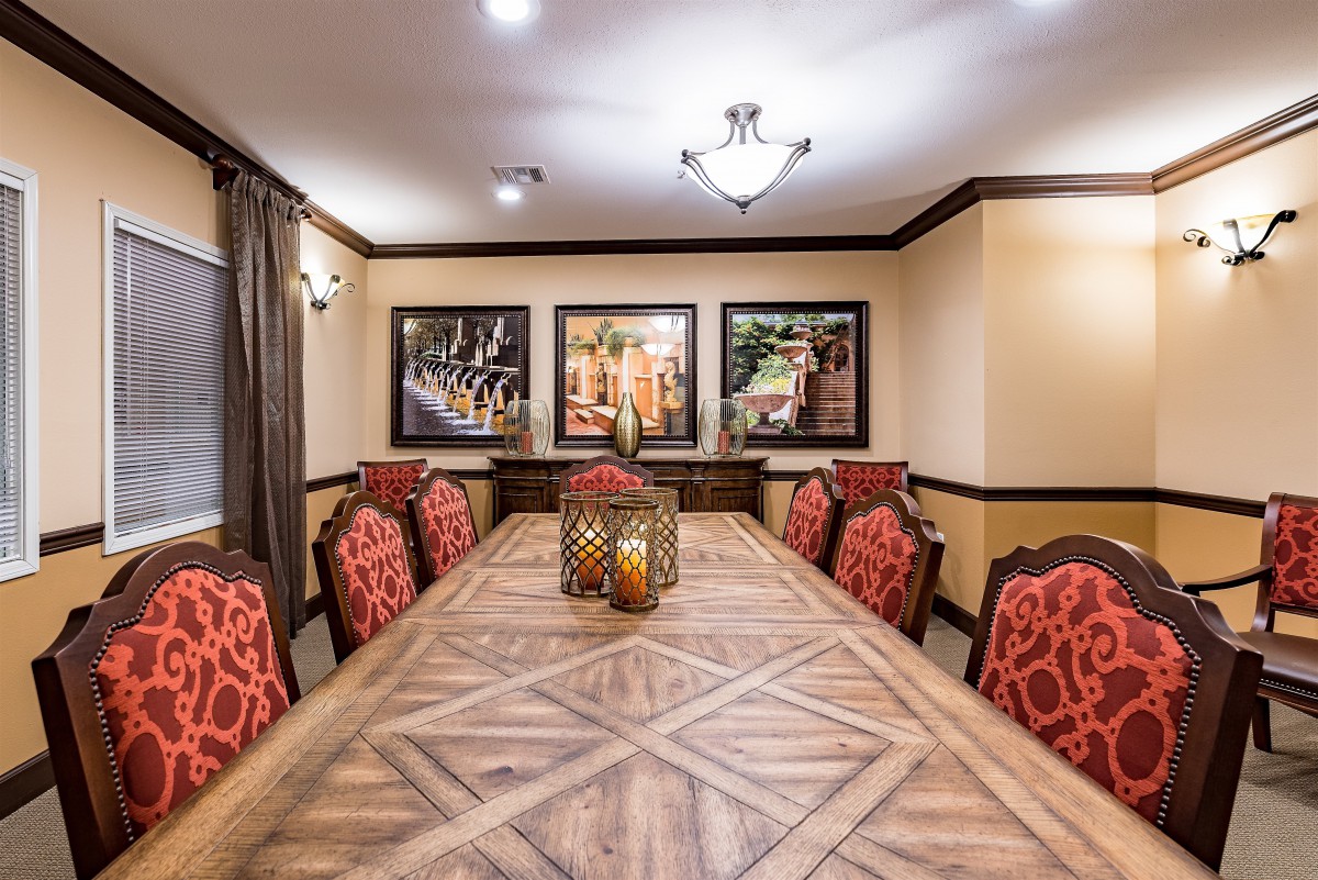A tastefully decorated dining room featuring a long wooden table surrounded by red upholstered chairs, with framed artwork on the walls.