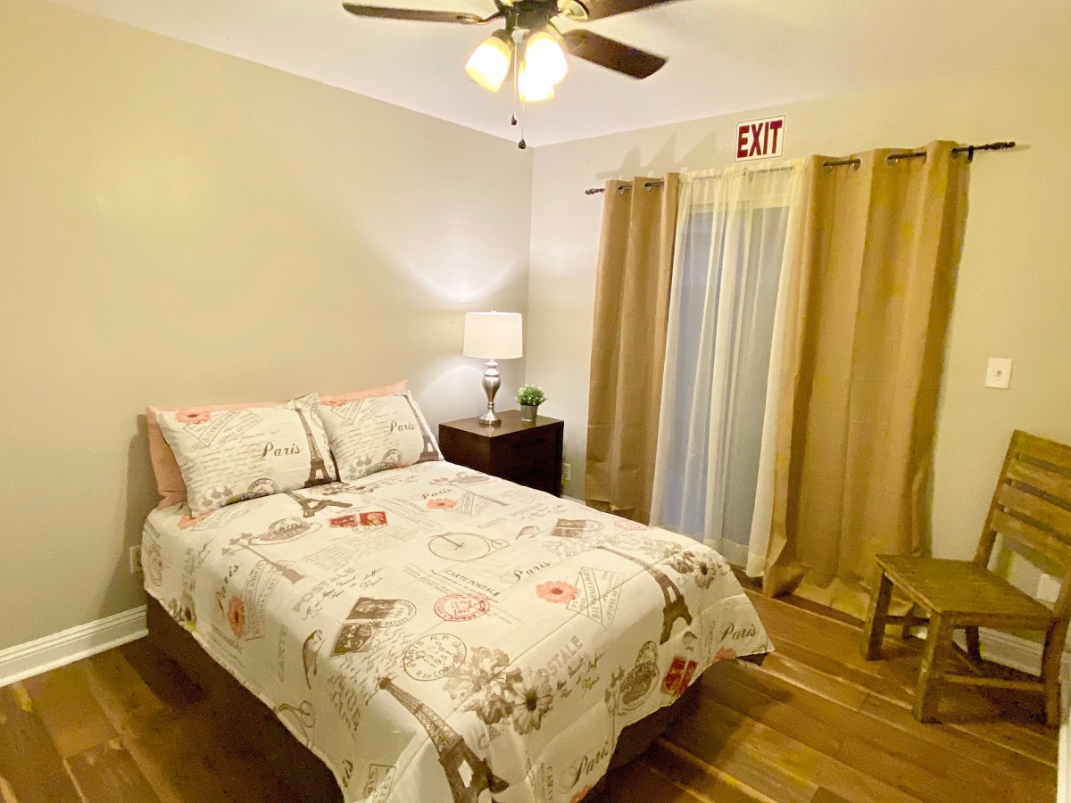 A cozy bedroom with a neatly made bed, wooden flooring, and warm lighting.