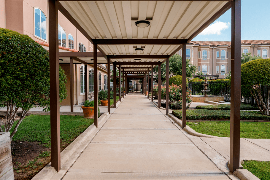 A covered walkway leading through a garden area, flanked by buildings.