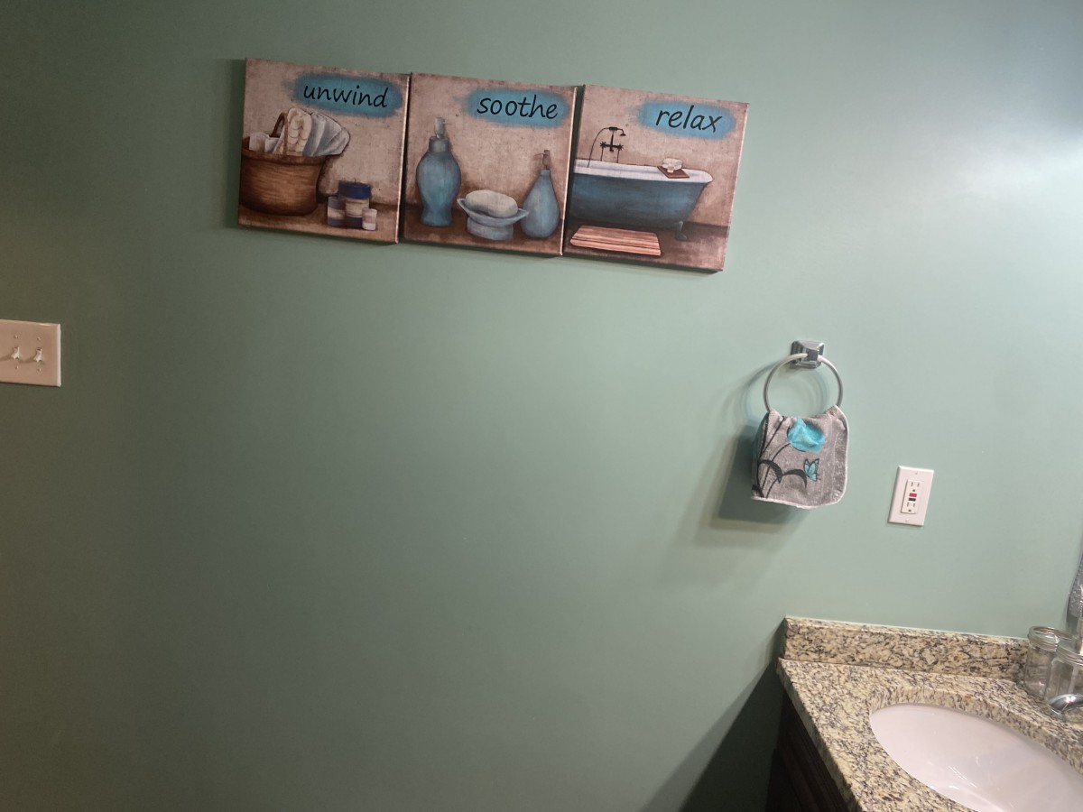 A bathroom with green walls features wall art and a towel holder near the sink.