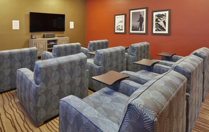 A cozy home theater room with multiple armchairs facing a large screen TV and decorated with framed pictures on the wall.