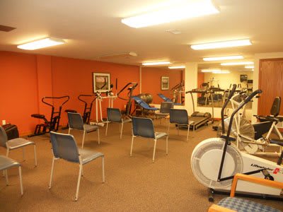 An indoor gym featuring various exercise equipment and chairs arranged in a well-lit room.