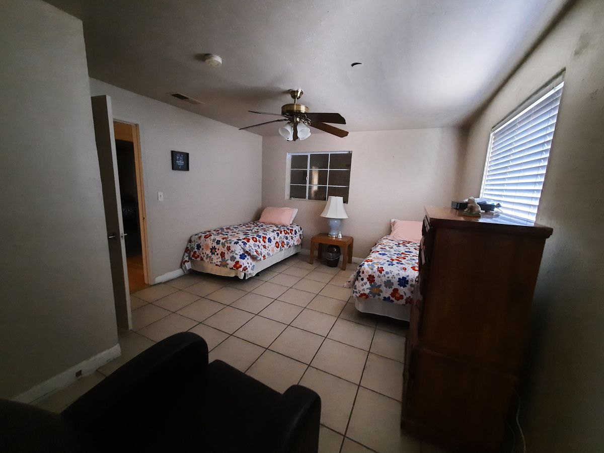 A simple bedroom with two single beds, a ceiling fan, and a tiled floor.