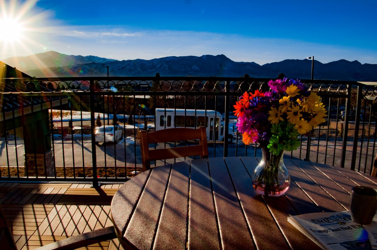 A scenic balcony view overlooking mountains at sunset, with a table and a colorful bouquet of flowers.