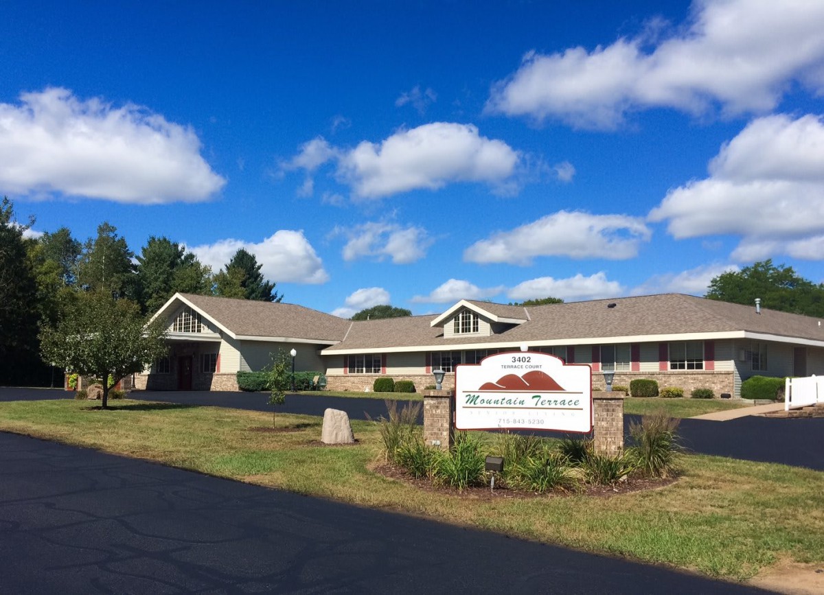 A healthcare facility with a sign in front, set against a clear blue sky with scattered clouds.