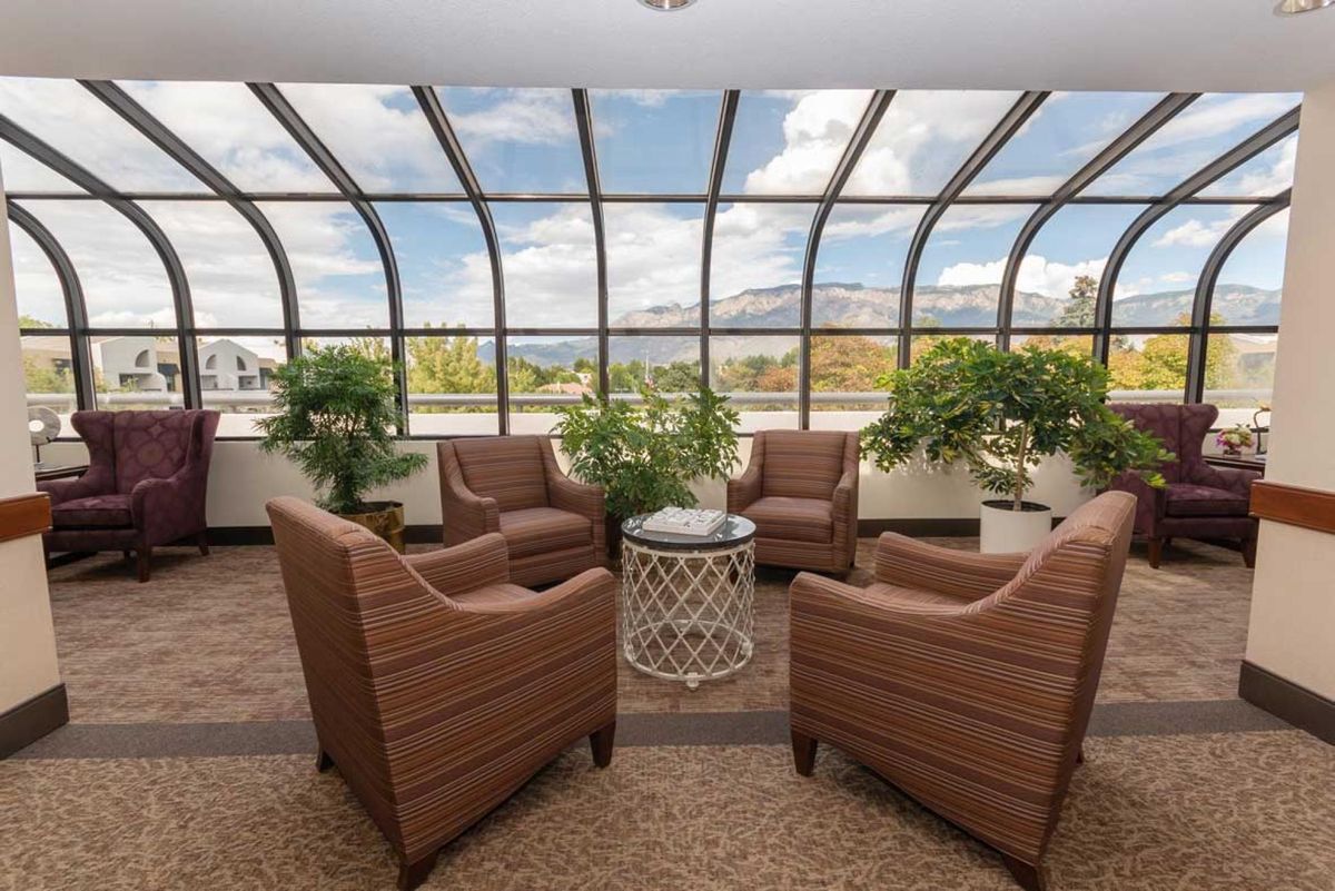 A cozy seating area in a glass-enclosed atrium with a scenic sky view.