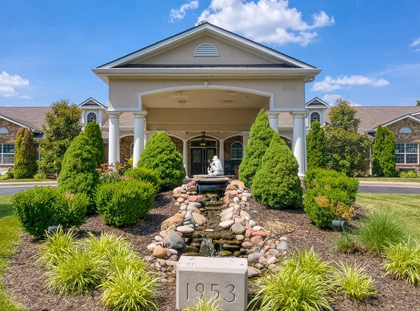 A building entrance with a landscaped garden and fountain in front.