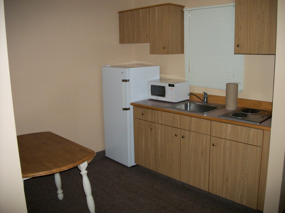 A simple kitchen setup with a refrigerator, microwave, sink, and wooden cabinets.