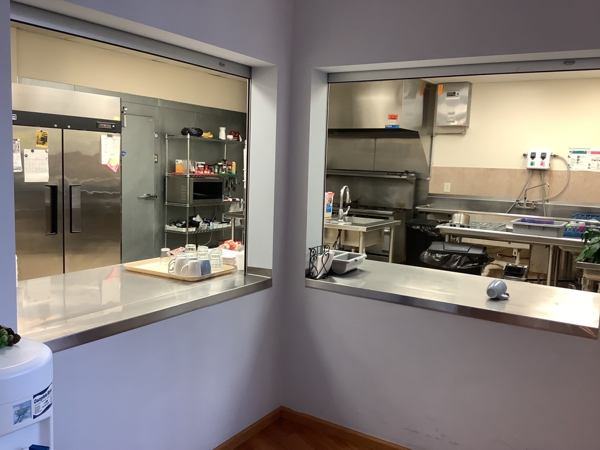 View of a commercial kitchen with stainless steel appliances and open service windows.