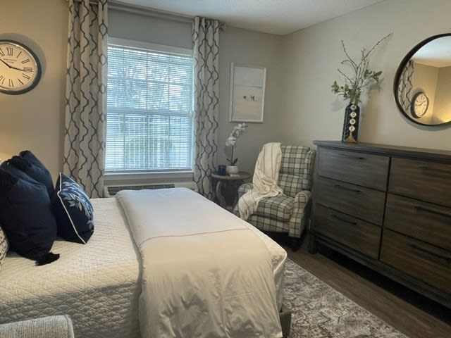 A cozy bedroom with elegant decor, featuring a large bed, a dresser, and a comfortable chair by the window.