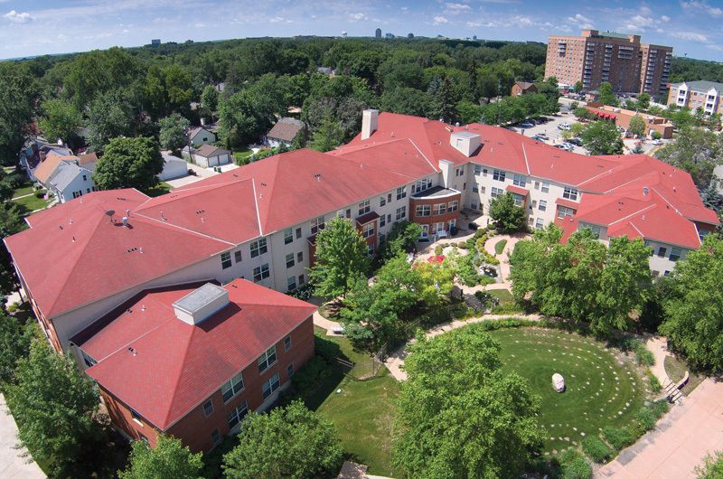 An aerial view of a large building with red rooftops, surrounded by green trees and garden areas.