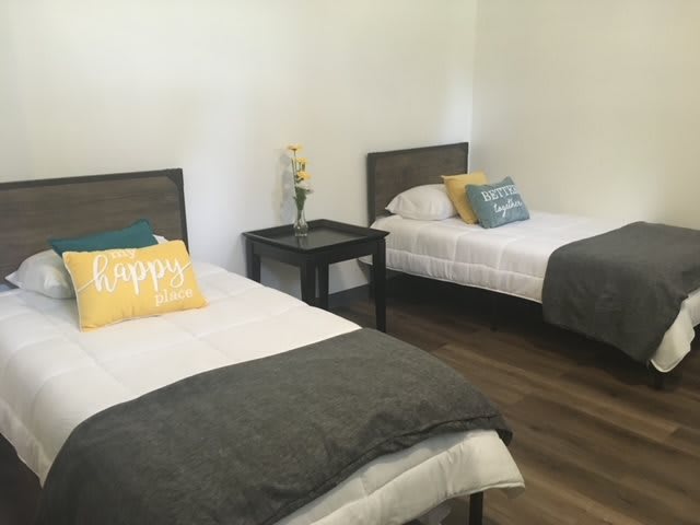 A minimalist bedroom with two beds, each adorned with pillows and a nightstand in between.