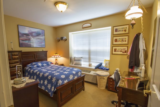A cozy bedroom with a wooden bed, desk, and a large window allowing natural light.
