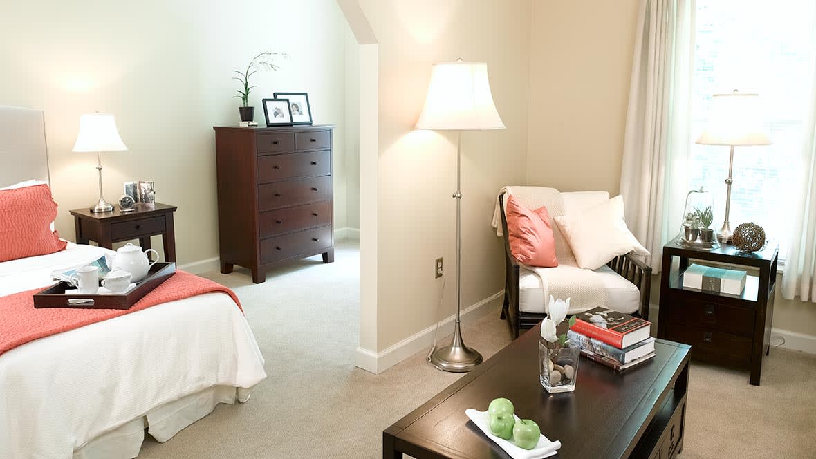 A cozy bedroom with a lamp, chair, and dresser.