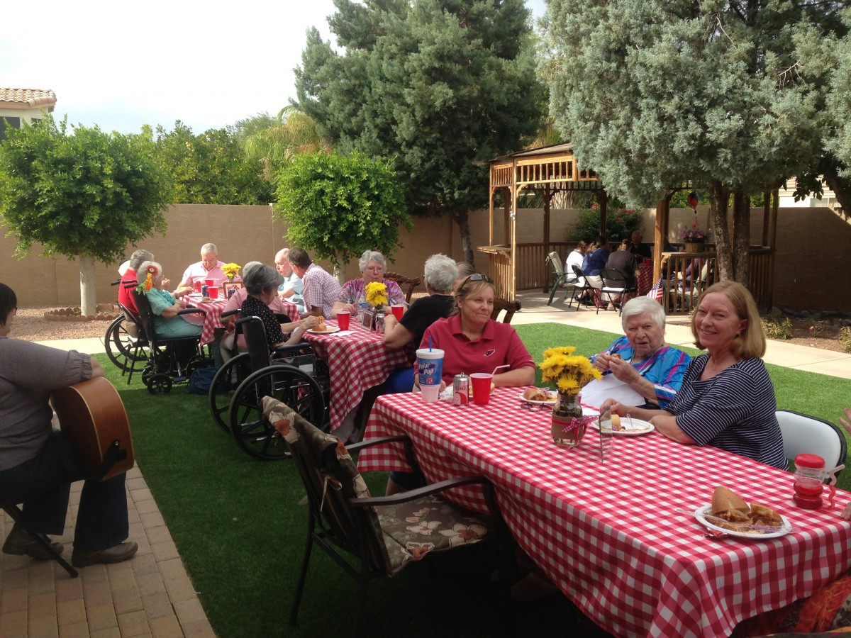 A group of elderly individuals enjoying an outdoor picnic with red and white checkered tablecloths in a garden setting.