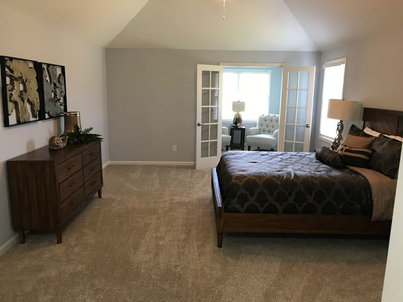 A spacious bedroom with a bed, dresser, and large windows allowing natural light.