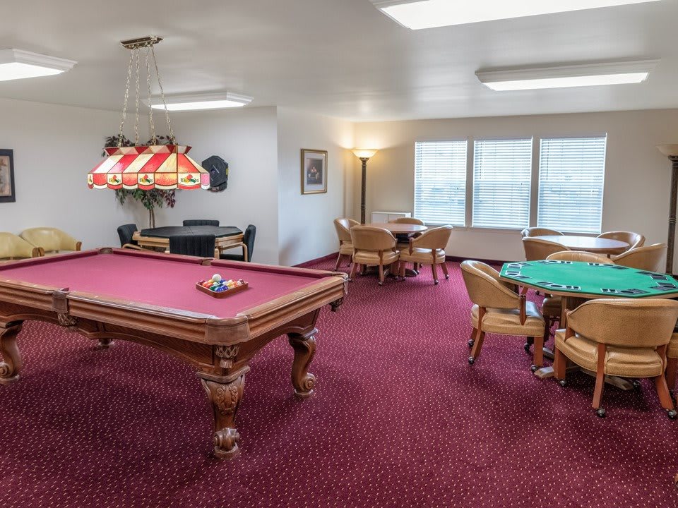 A recreational game room featuring a pool table and multiple card tables on a red-carpeted floor.