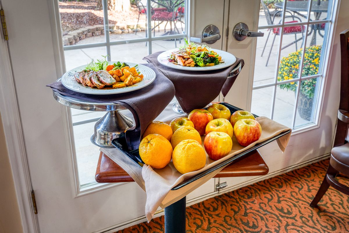 A dining area setup with plates of food and a tray of fresh apples and oranges.
