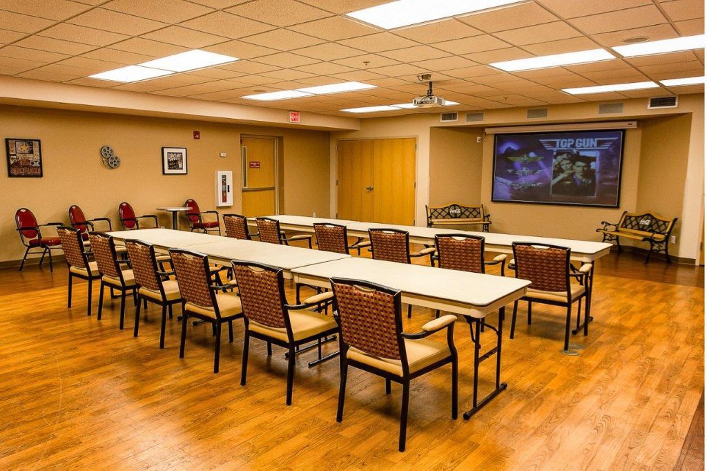 A conference room with arranged tables and chairs, featuring a projector screen.