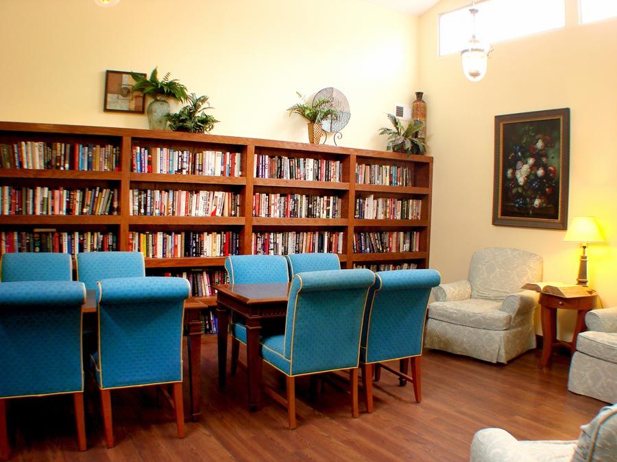A cozy library space featuring a large bookshelf, a table with blue chairs, and a comfortable armchair.