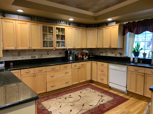 A modern kitchen featuring wooden cabinets, black countertops, and a decorative rug.