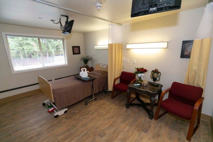 A hospital room with a patient bed, seating area, and TV.