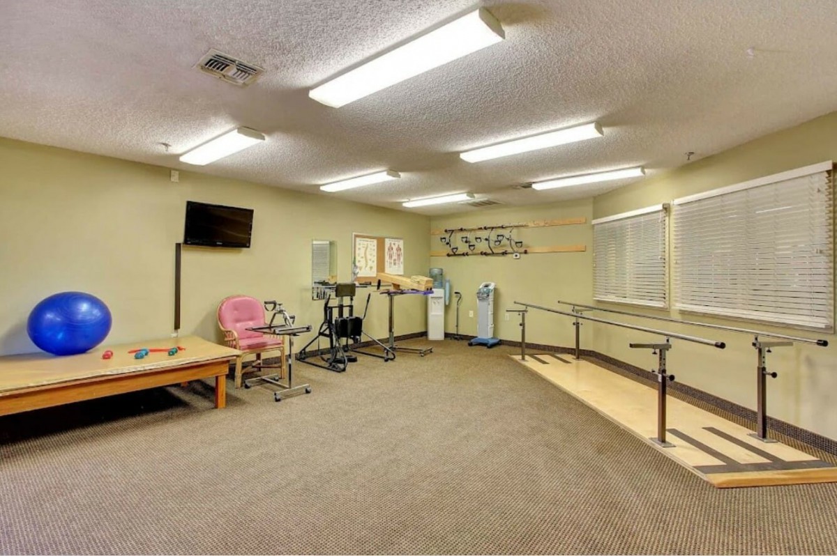 A rehabilitation room equipped with exercise machines and parallel bars for physical therapy.