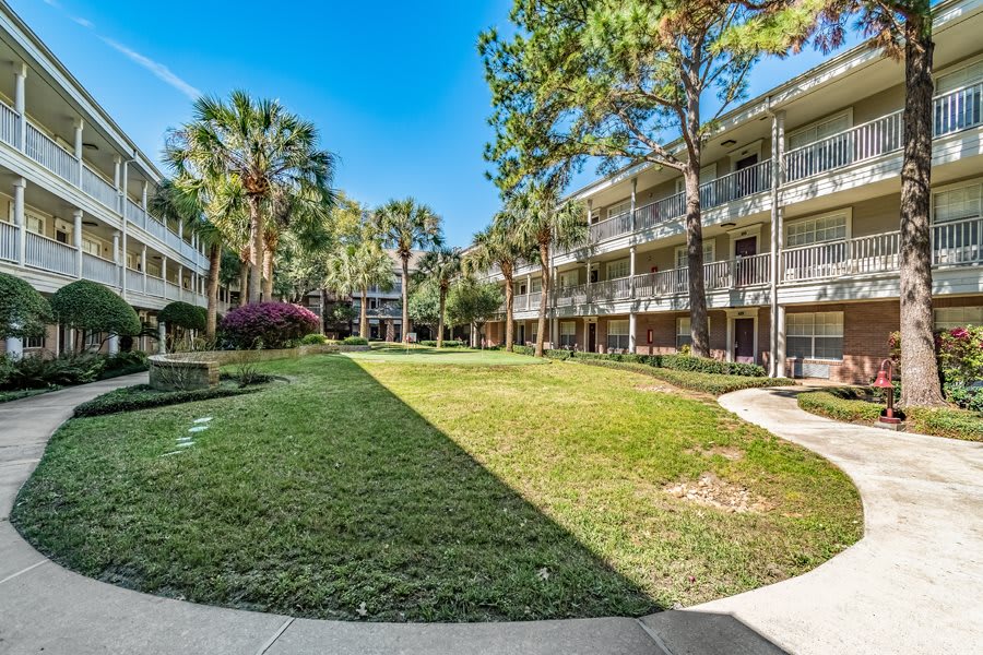 A view of an apartment complex with surrounding greenery and a well-maintained lawn.