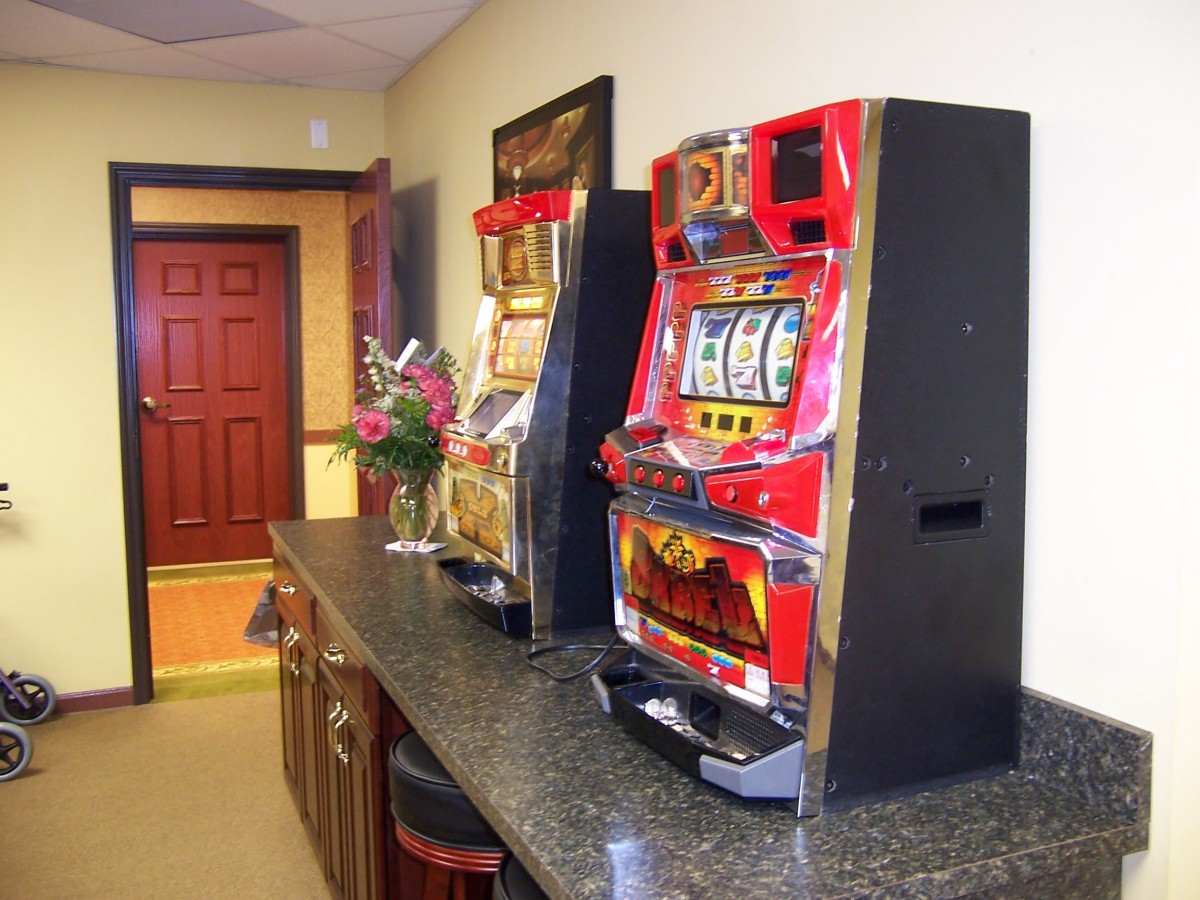 A lobby area with slot machines on a counter, featuring a red door and a flower arrangement.