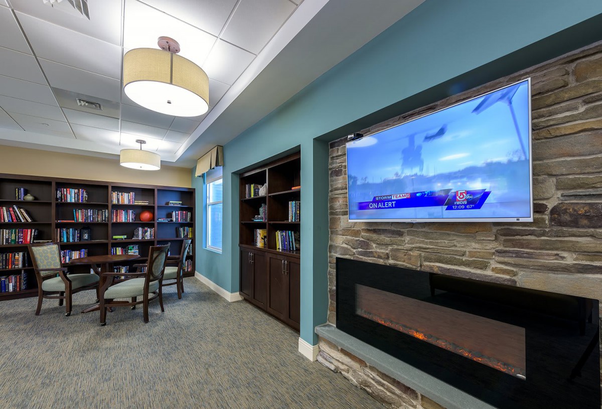 A cozy library corner with bookshelves, a television above a fireplace, and soft lighting.