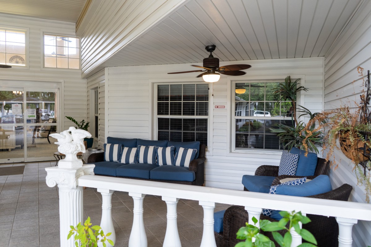 A cozy porch with comfortable seating and a ceiling fan surrounded by greenery.