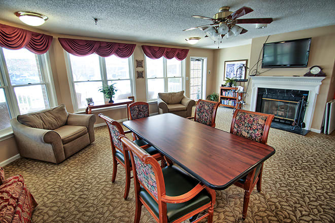 A cozy living room featuring a dining table with chairs, comfortable sofas, a fireplace, and large windows.