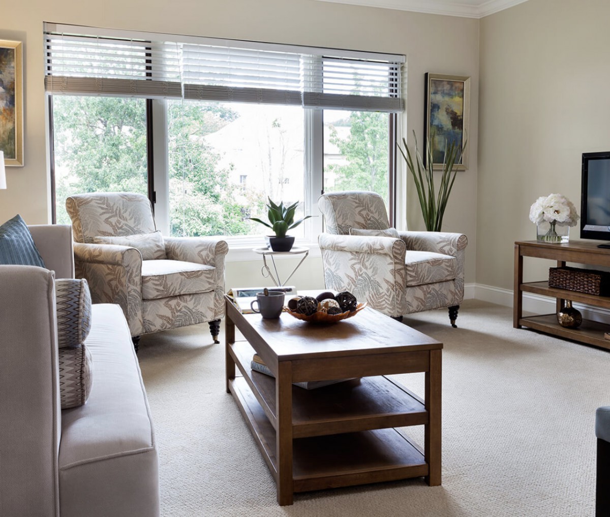 A modern and minimalist living room with large windows allowing natural light to illuminate the space, featuring comfortable seating, a wooden coffee table, and decorative plants.