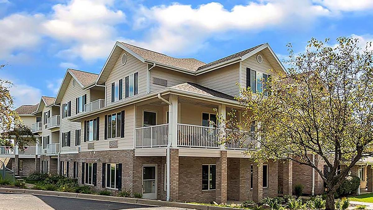 A residential building with a porch and multiple windows under a partly cloudy sky.