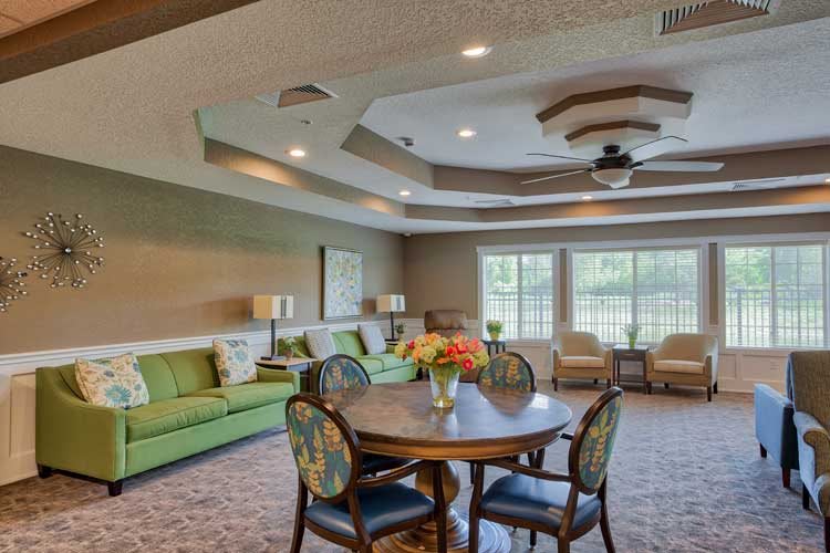 A cozy living room with stylish furniture, including a round table and chairs, sofas, and a ceiling fan.