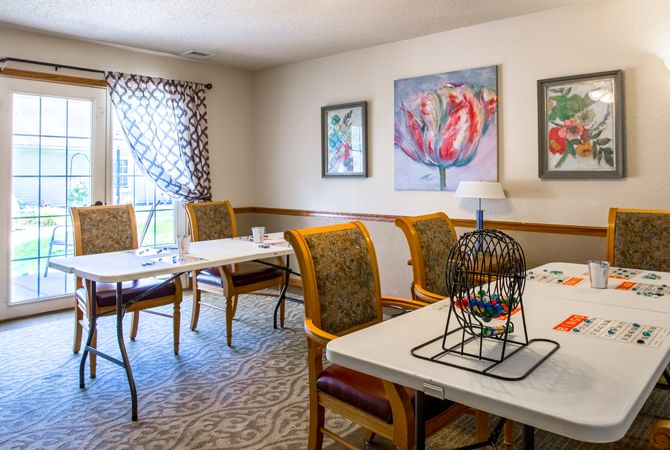 A cozy dining room with tables, upholstered chairs, and colorful artwork on the walls.